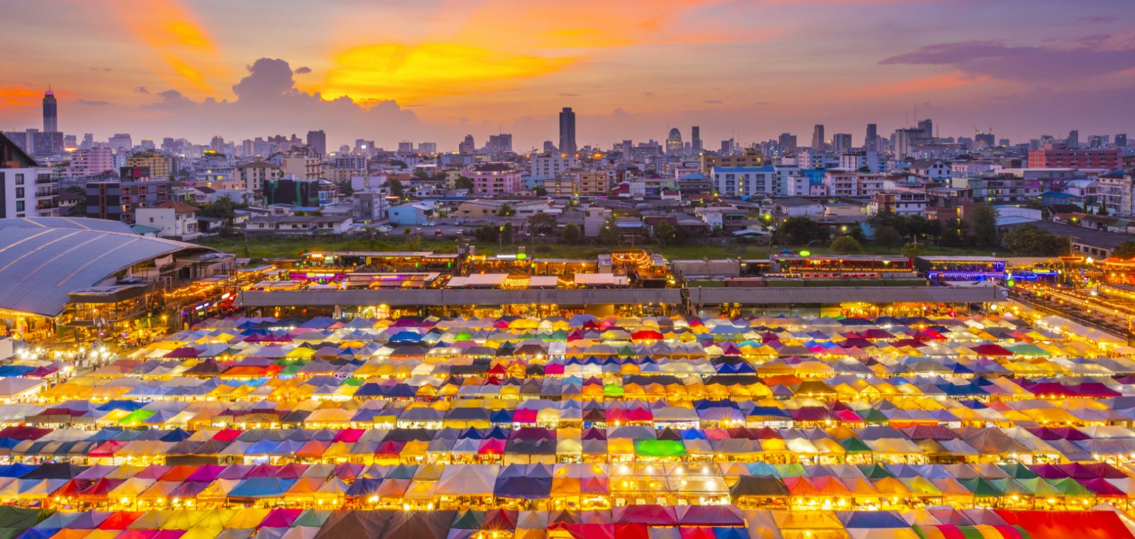 Colorful market rooftops glowing at sunset beneath a city skyline